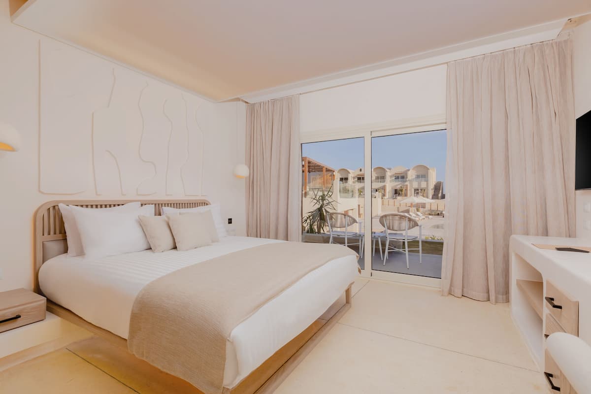 A modern hotel room with a large bed, a desk, and a balcony with a view of the city.