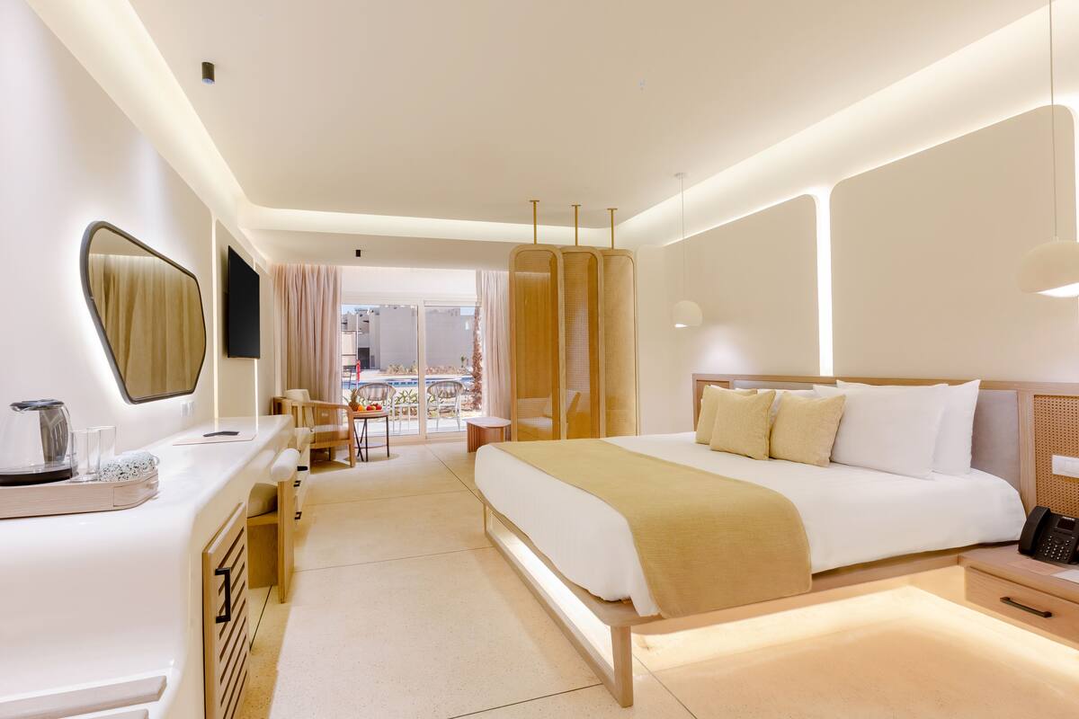 A modern hotel room with a large bed, bedside table, and a view of the city.
