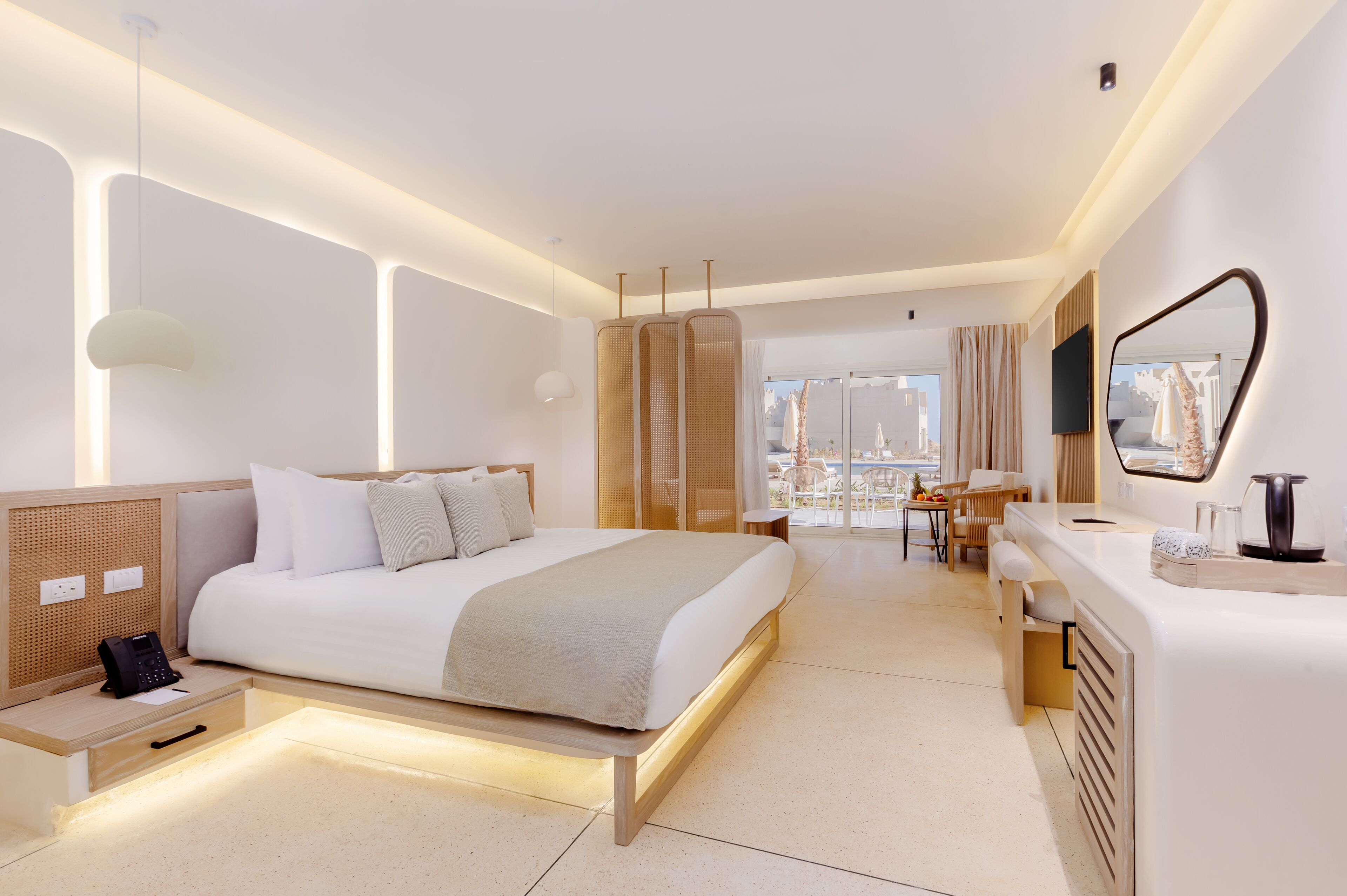 Ein modernes Hotelzimmer mit einem großen Bett, einem Nachttisch und einem Schreibtisch mit Stuhl. Ein großes Fenster bietet Blick auf die Stadt.