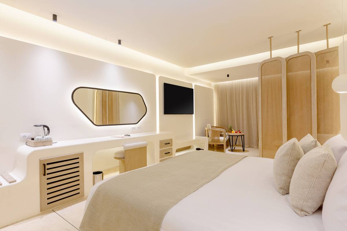 A modern hotel room with a large bed, a bedside table, a desk, a chair, a TV, and a window with curtains.