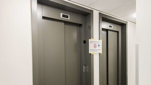 Un pasillo con tres puertas de ascensor, una lámpara en el techo y un cartel que prohíbe fumar.