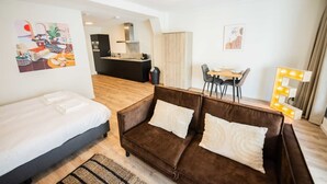 Una habitación de hotel moderna con una cama, un sofá marrón, una zona de comedor y una cocina al fondo.