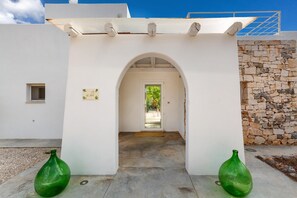 Un edificio blanco con un muro de piedra, una puerta y dos macetas verdes.