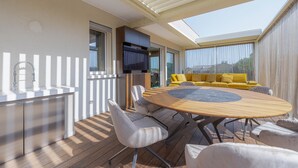 A modern outdoor dining area with a wooden table and chairs, a built-in grill, and a yellow sofa. - Venice New Luxury Penthouse with parking (Mestre)