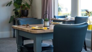 A dining table with chairs, a plant, and a window with curtains. - The Clifton Hotel (Morecambe)