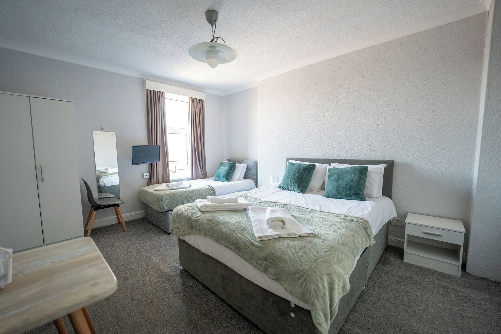 A hotel room with two beds, a desk, a chair, a TV, and a window with curtains.