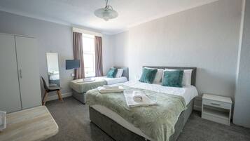 A hotel room with two beds, a desk, a chair, a TV, and a window with curtains.