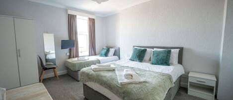 A hotel room with two beds, a desk, a chair, a TV, and a window with curtains.