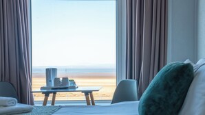 A hotel room with a bed, a table with a tray of items, and a view of the beach. - The Clifton Hotel (Morecambe)