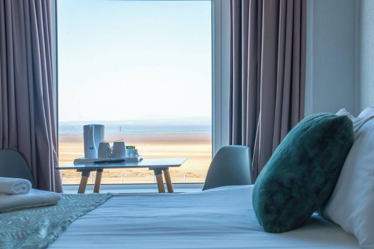 A hotel room with a bed, a table with a tray of items, and a view of the beach.