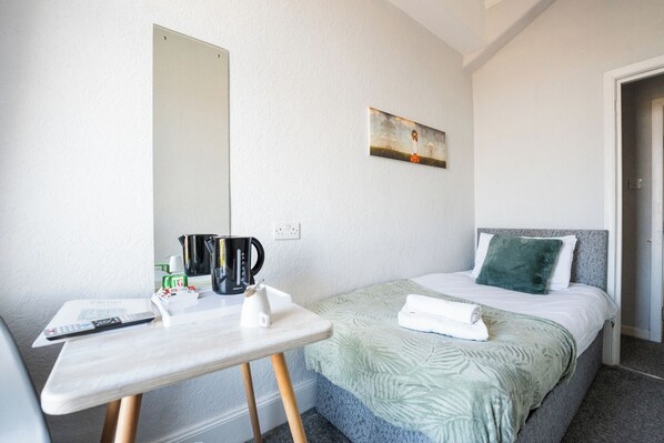 A hotel room with a bed, a bedside table, a painting on the wall, and a kettle on the table. - The Clifton Hotel (Morecambe)