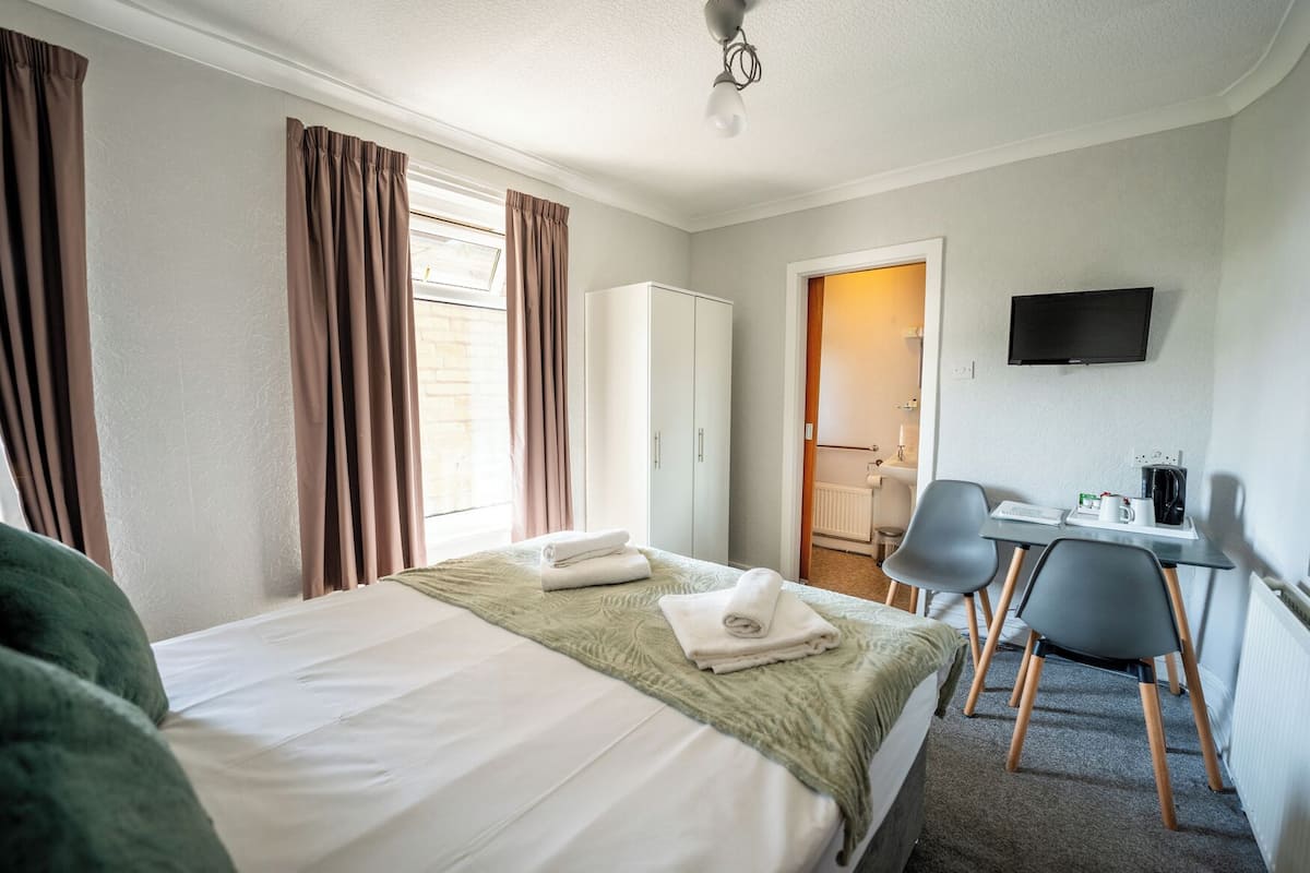 A hotel room with a bed, a desk with a chair, a television, and a bathroom visible through an open door.
