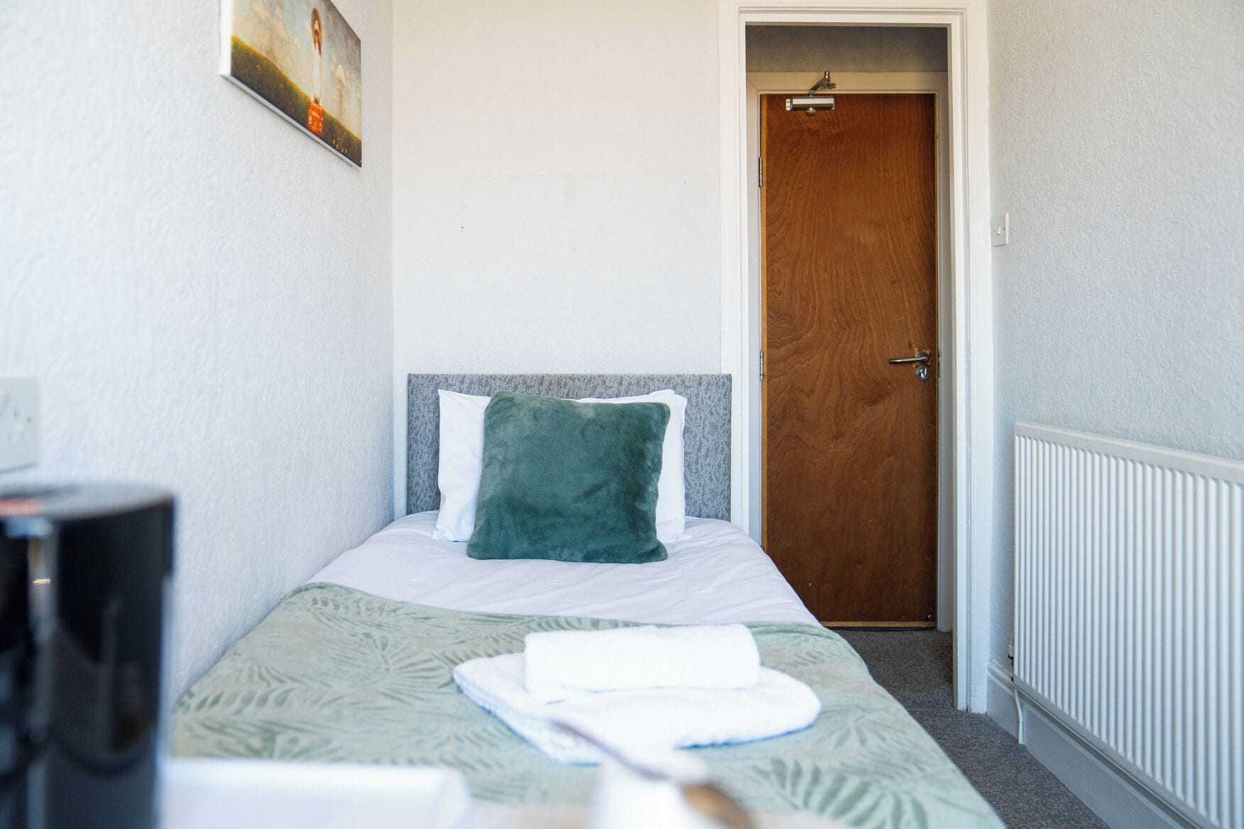 Un dormitorio pequeño y ordenado con una cama individual, una puerta de madera y un radiador.