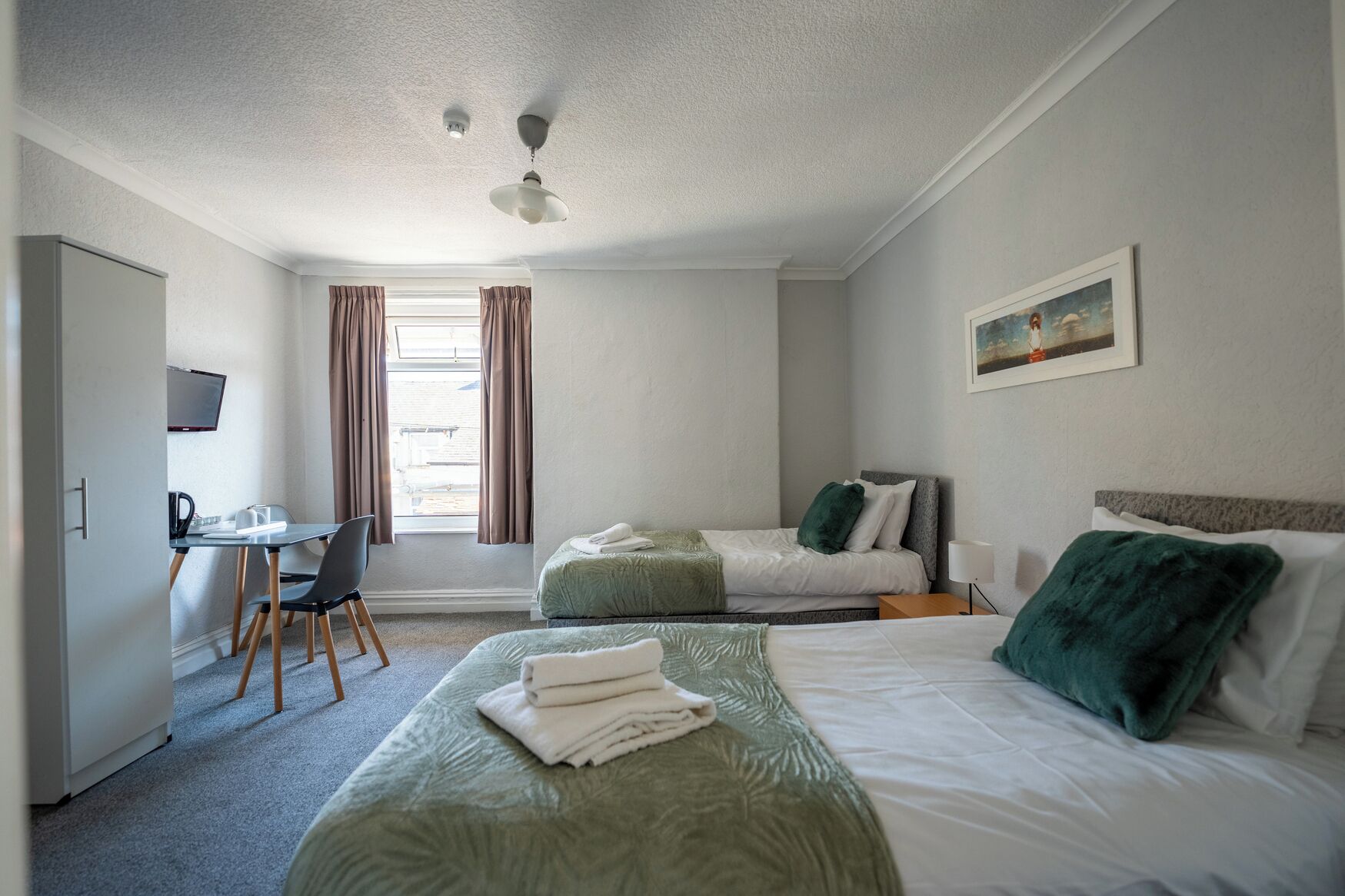 A hotel room with two beds, a desk, a chair, and a television.