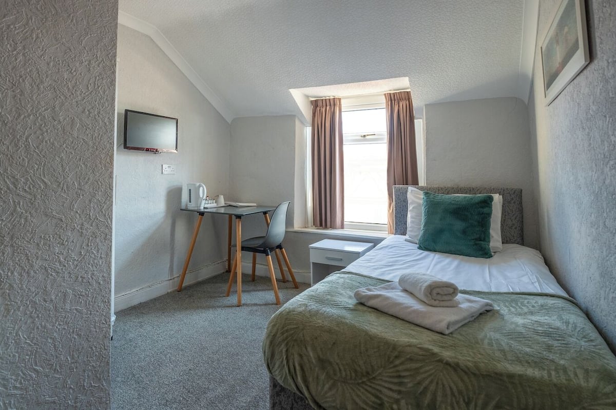A small, neatly arranged room with a bed, a desk, and a chair.