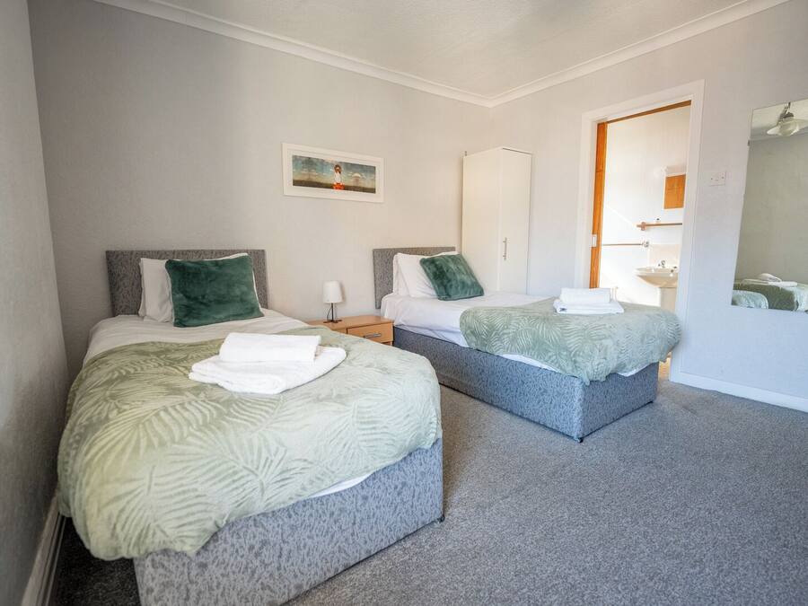 A hotel room with two beds, a small bedside table with a lamp, a wardrobe, and a mirror on the wall.