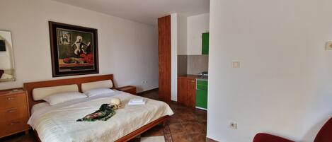 Une chambre d’hôtel comprenant un lit, une table de chevet, un tableau, une armoire en bois et une kitchenette.