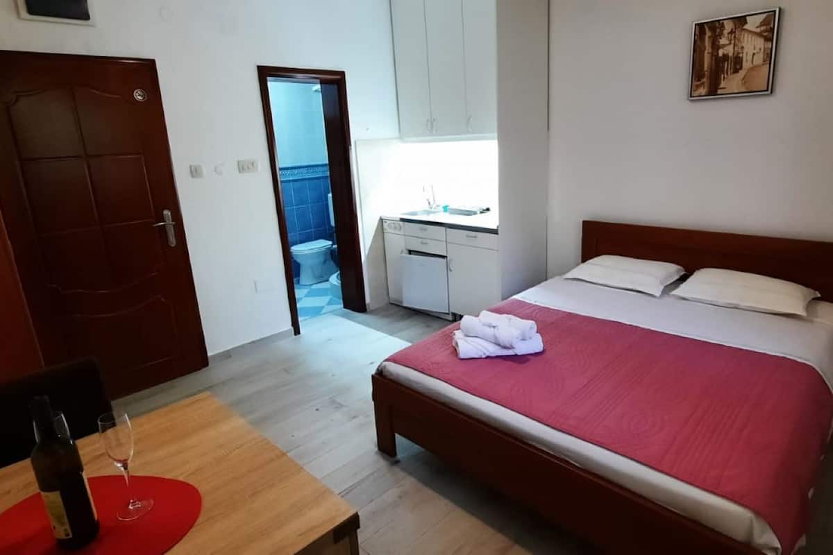 A hotel room with a bed, a desk with a chair, a red rug, and a door leading to a bathroom.