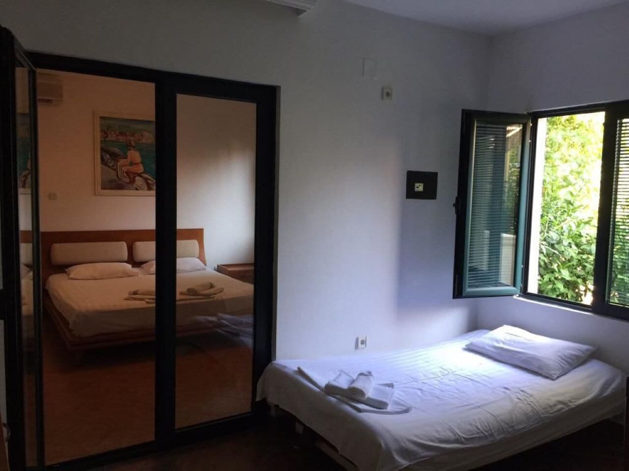 Een slaapkamer met een bed, een raam met zonwering, een deur naar een andere kamer en een schilderij aan de muur.