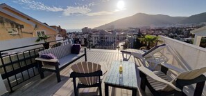 A rooftop terrace with a table, chairs, and a sofa, overlooking a cityscape and mountains. - Villa Lutovac (Budva)