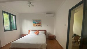 A bedroom with a wooden bed, white bedding, a painting on the wall, and a small table with chairs. - Villa Lutovac (Budva)