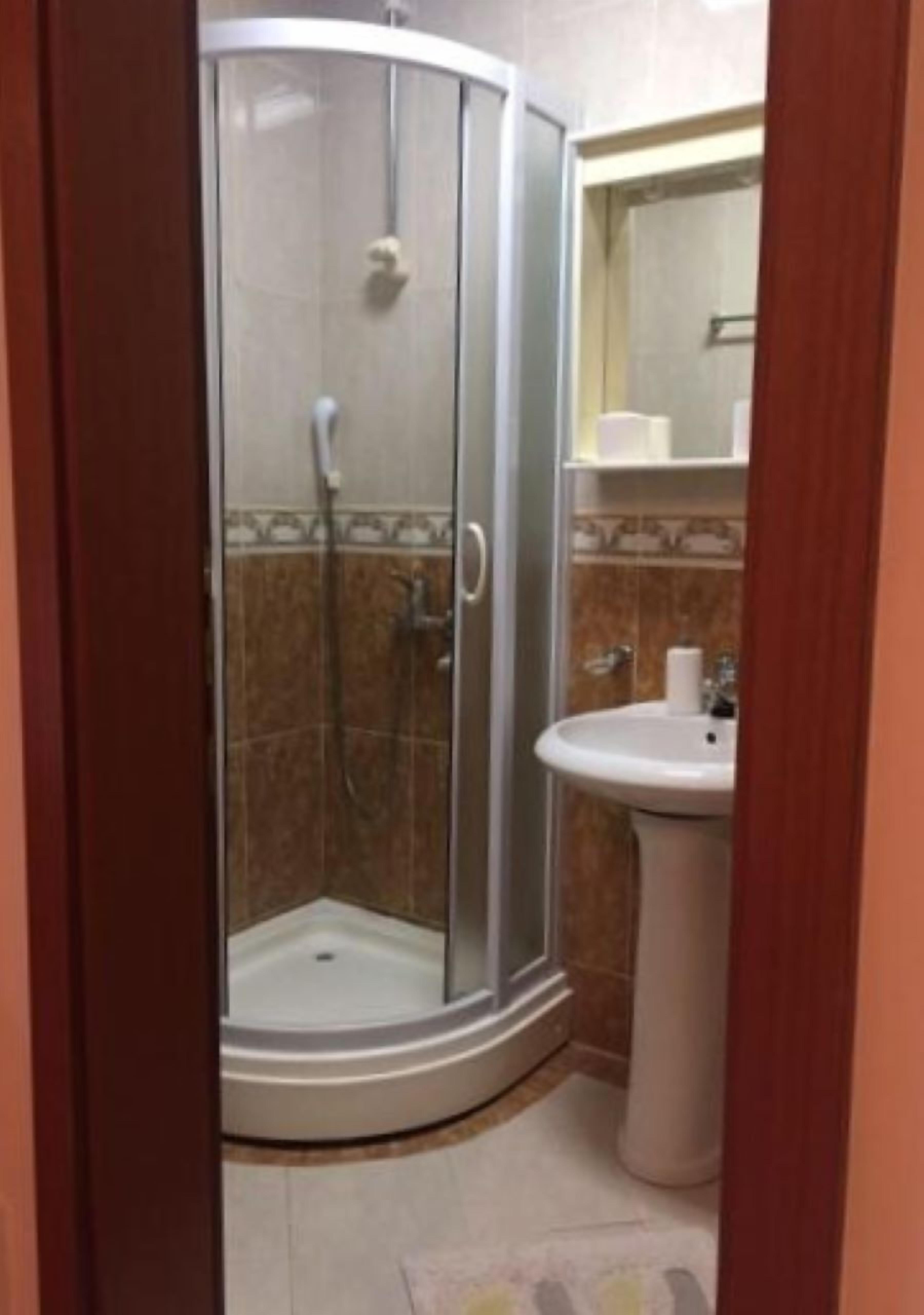 Baño con ducha envuelta en vidrio, lavamanos sobrepedestal y salpicadero de azulejos.