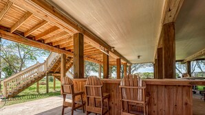 Une terrasse en bois avec un coin bar, des sièges extérieurs et un escalier menant à un niveau supérieur.