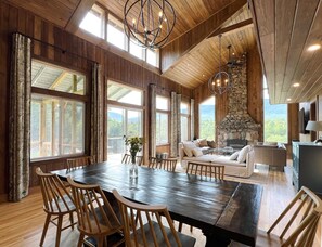A spacious dining area with a large wooden table and chairs, a stone fireplace, and large windows offering a view of the outdoors. - Spectacular Views, Private River Access Home (Wilmington)