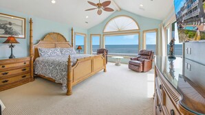Un dormitorio amplio con una cama grande, ventilador de techo, vista al océano y un ventanal.