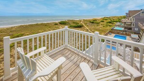 Una terraza de madera con barandillas blancas que da a una playa y al océano.