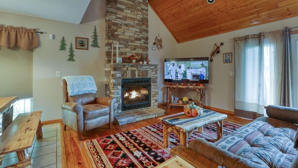 A cozy living room with a stone fireplace, wooden ceiling, and a television.