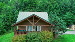 A small cabin with a porch, surrounded by lush greenery.