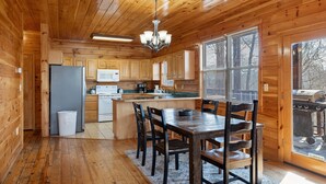A wooden cabin kitchen with a central island, wooden cabinets, a refrigerator, a microwave, and a dining table with chairs.