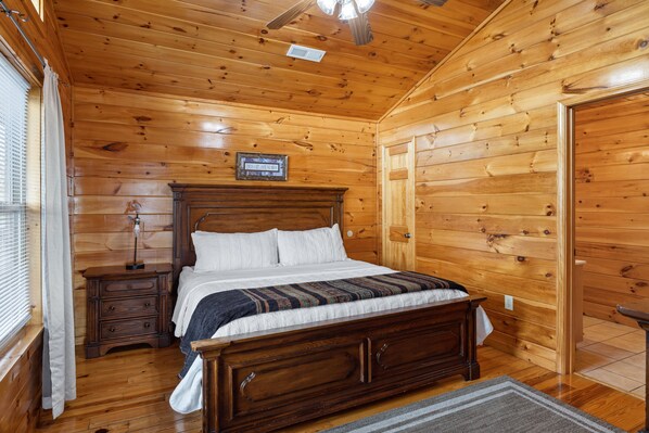 A wooden-paneled bedroom with a bed, nightstand, and a ceiling fan.