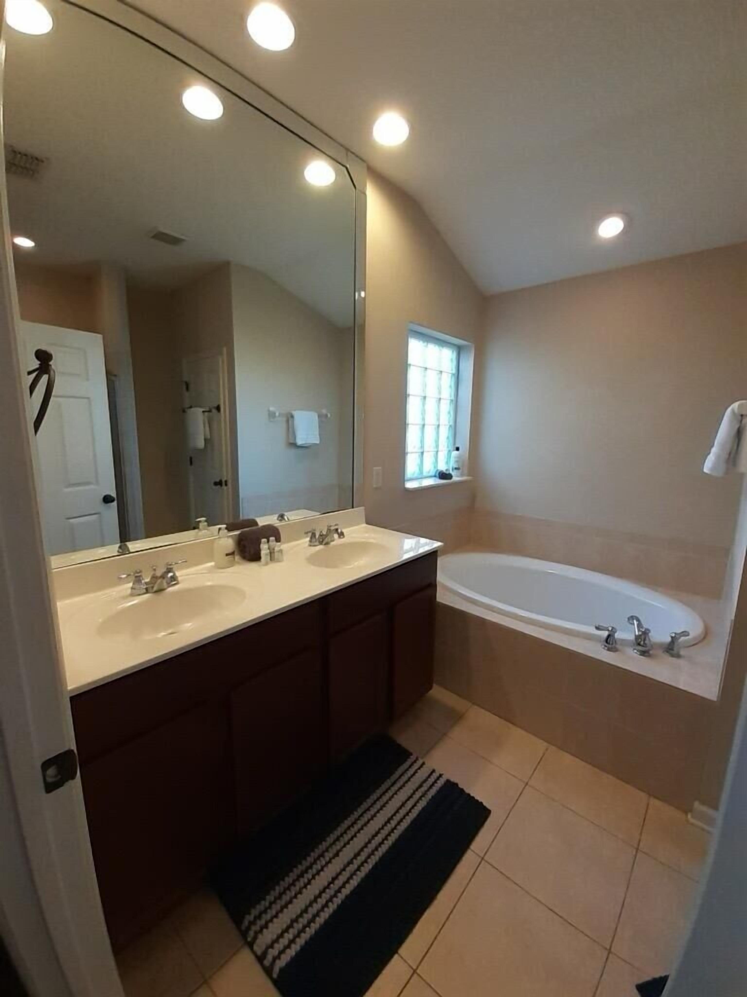 Un baño moderno con dos lavamanos, un espejo grande, una bañera y una ventana.