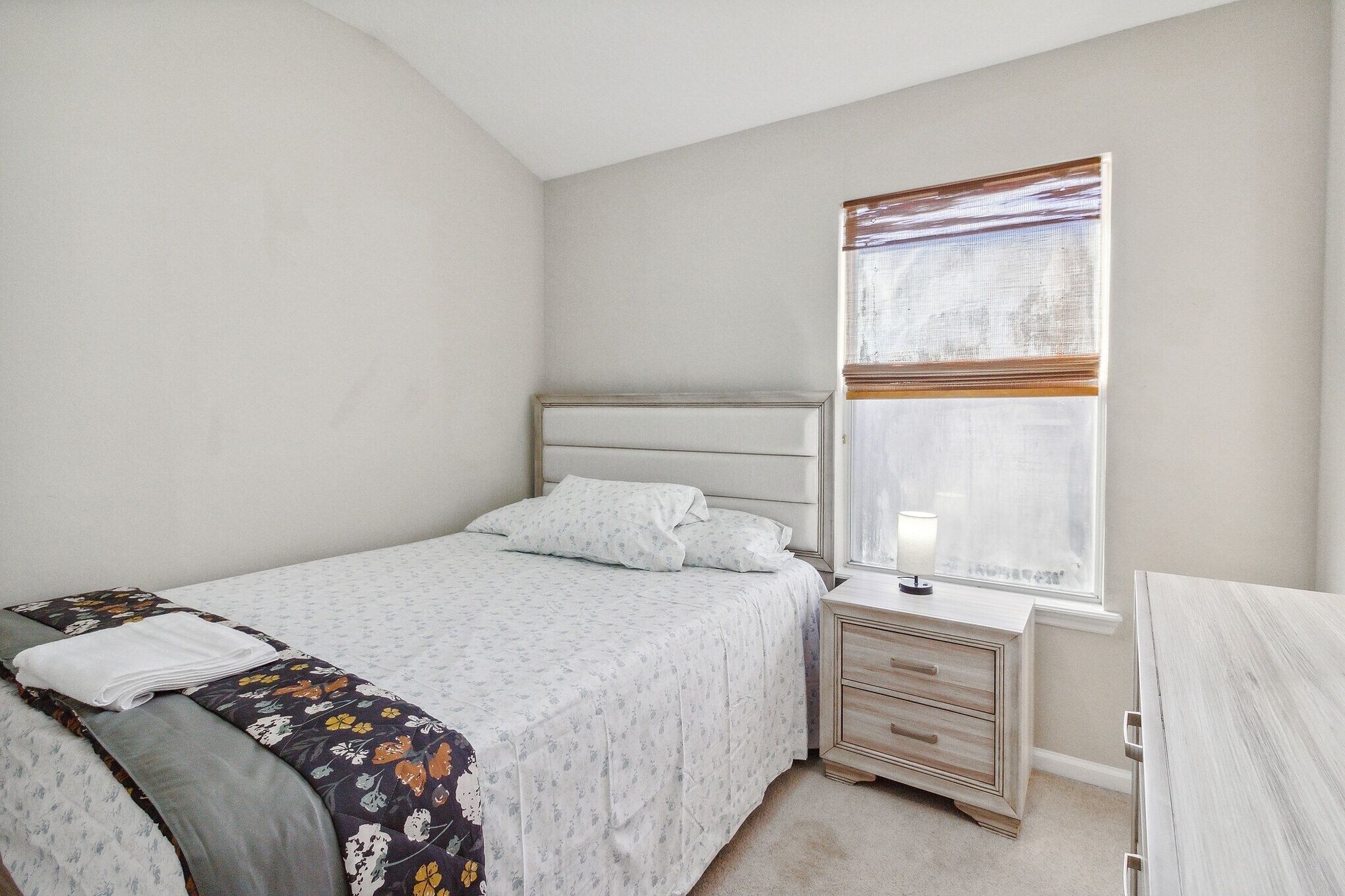 A bedroom with a bed, bedside table, and a window with blinds.