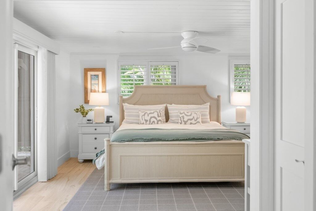 A bedroom with a bed, two bedside tables, a nightstand, a ceiling fan, and a window with blinds.