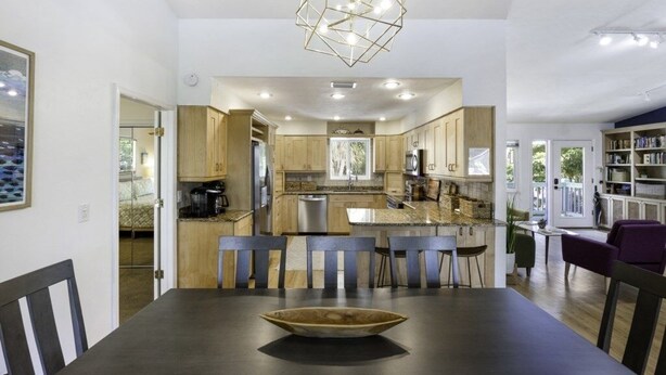 Een moderne keuken met houten kastjes, een centraal eiland en een eethoek met een donkere tafel en stoelen.