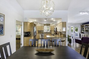 Una cocina moderna con armarios de madera, una isla central y un comedor con una mesa y sillas oscuras.