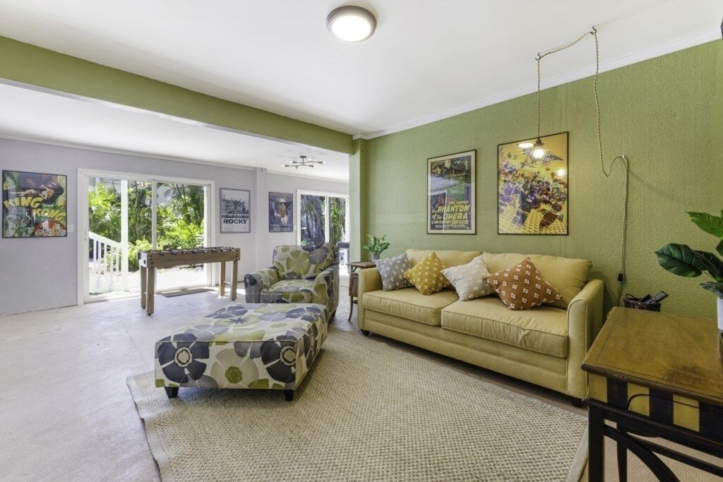 Un salon avec un canapé, un pouf et une table basse. Il y a des affiches au mur et une plante sur la droite.