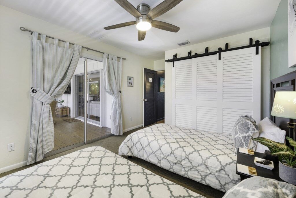 A bedroom with two beds, a ceiling fan, a sliding door, and a nightstand with a lamp.