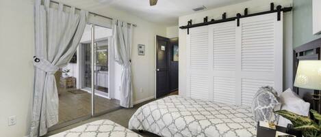 A bedroom with two beds, a ceiling fan, a sliding door, and a nightstand with a lamp.