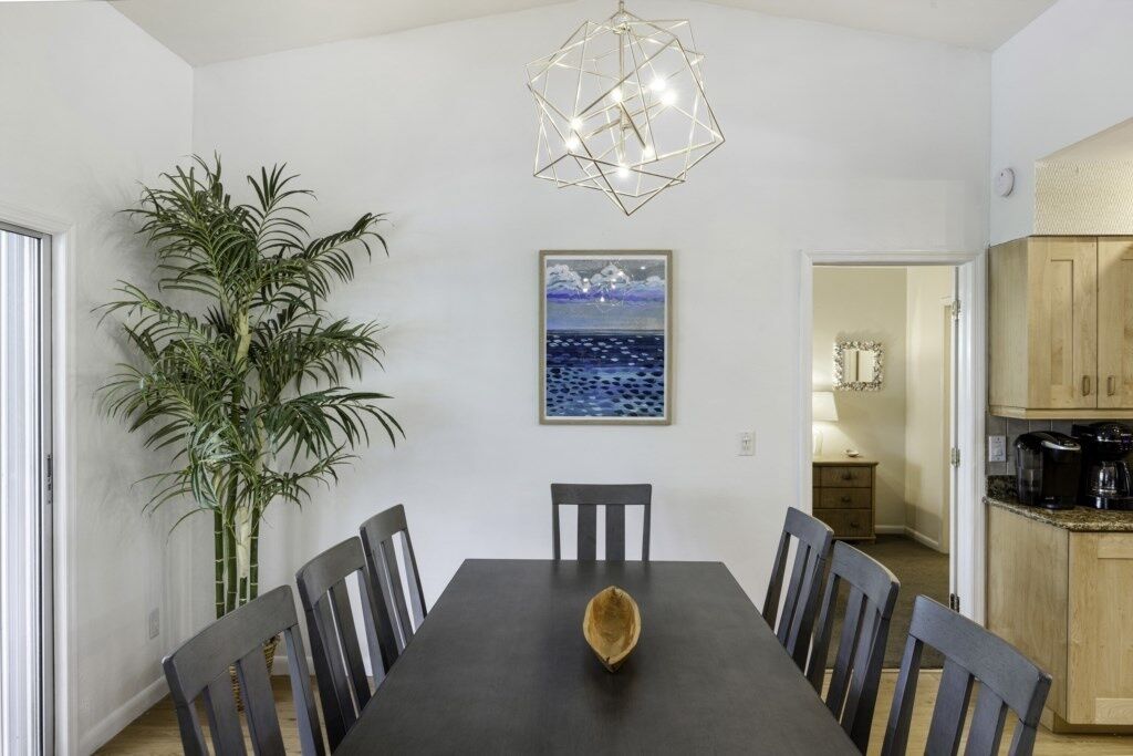 A dining area with a dark wooden table, six chairs, a large potted plant, and a geometric light fixture above.
