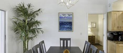 A dining area with a dark wooden table, six chairs, a large potted plant, and a geometric light fixture above.