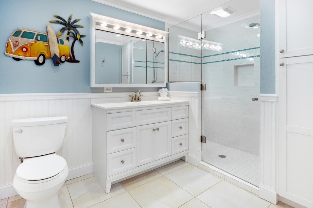 A bathroom with a white vanity, a toilet, a glass shower enclosure, and a wall-mounted mirror with lights.