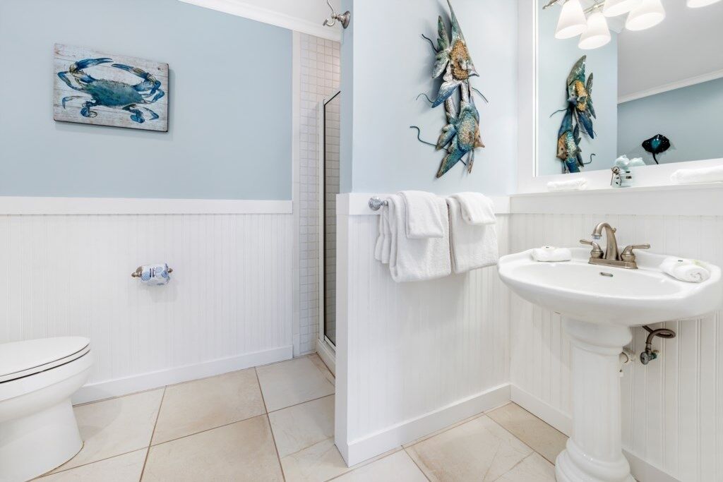 Un baño con inodoro blanco, lavamanos y ducha. Hay toallas colgadas en la pared y un pez decorativo.