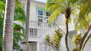 Un edificio de dos plantas con fachada blanca y detalles verdes, rodeado de palmeras.