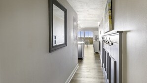 Un couloir avec un plancher en bois, un mur blanc et une porte donnant sur un espace cuisine.