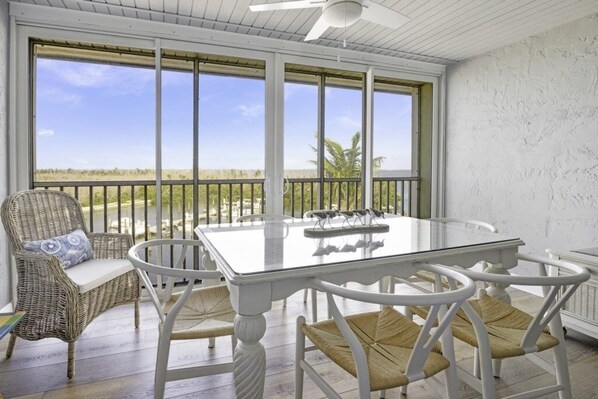 Überdachte Terrasse mit Glastisch und Korbstühlen, mit Blick auf einen Strand.