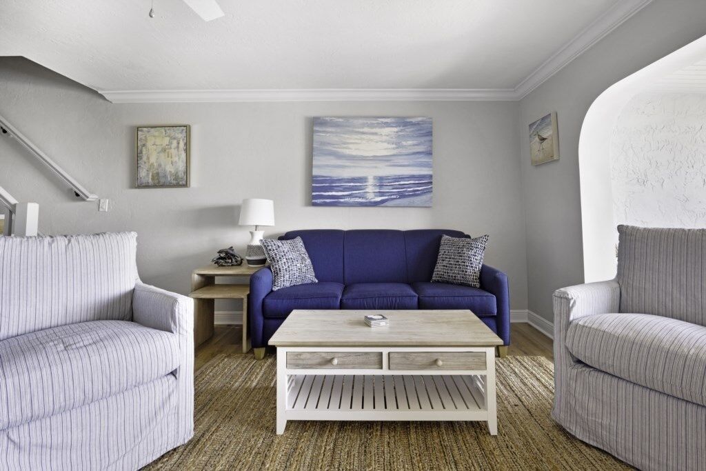 A living room with a blue sofa, two striped armchairs, a wooden coffee table, and a painting of a seascape.
